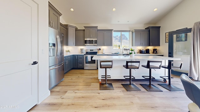 kitchen with appliances with stainless steel finishes, a breakfast bar area, light countertops, a sink, and light wood-style flooring