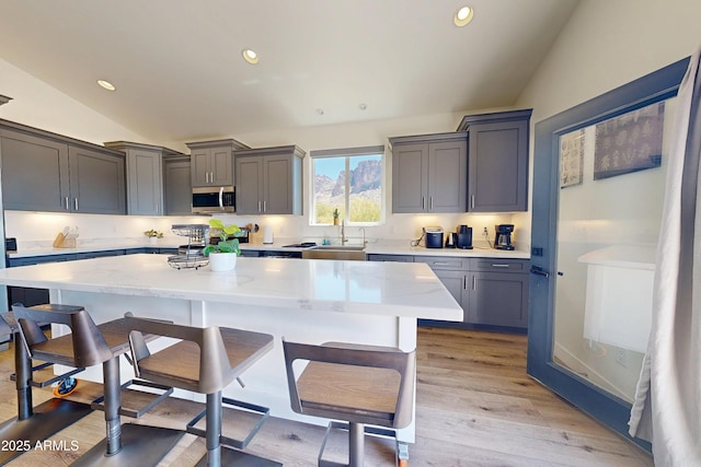 kitchen with stainless steel microwave, vaulted ceiling, a breakfast bar area, a kitchen island, and a sink