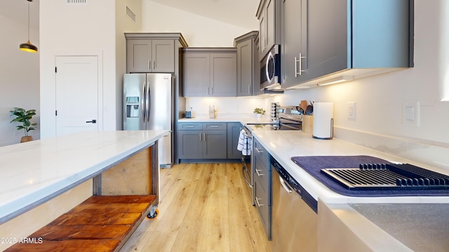 kitchen featuring stainless steel appliances, light wood finished floors, gray cabinetry, hanging light fixtures, and lofted ceiling