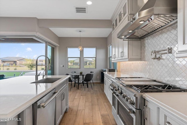 kitchen featuring pendant lighting, sink, wall chimney exhaust hood, light hardwood / wood-style flooring, and appliances with stainless steel finishes