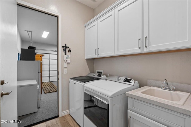 laundry room with cabinets, light hardwood / wood-style flooring, separate washer and dryer, and sink