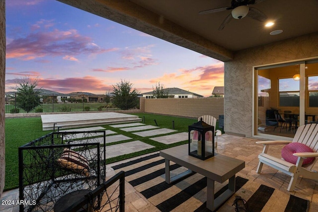 patio terrace at dusk featuring ceiling fan and a yard