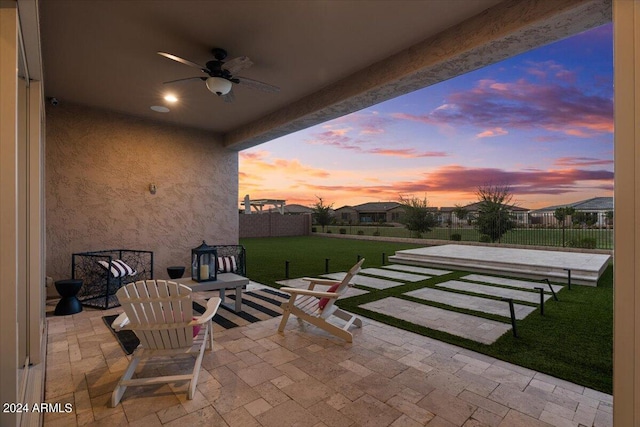 patio terrace at dusk featuring a yard and ceiling fan