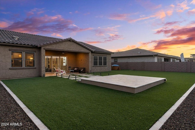 back house at dusk featuring a lawn and a patio