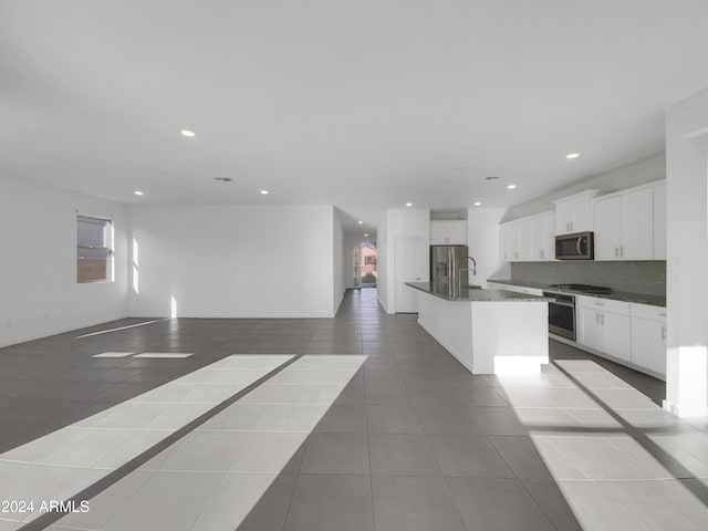 kitchen with a center island with sink, white cabinets, light tile patterned floors, tasteful backsplash, and stainless steel appliances