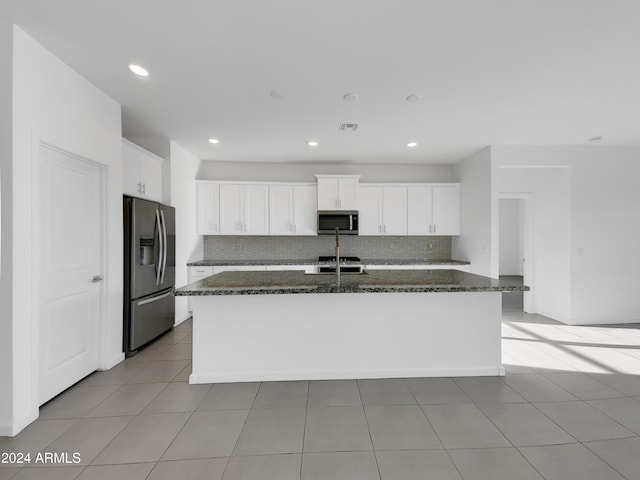 kitchen with stainless steel appliances, backsplash, dark stone countertops, an island with sink, and white cabinets