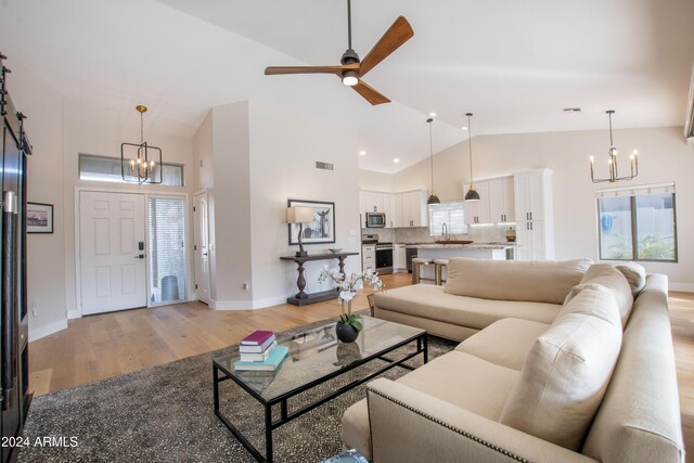 living room with ceiling fan with notable chandelier, light hardwood / wood-style floors, lofted ceiling, and sink