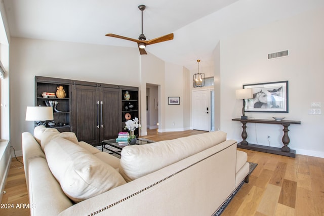 living room with ceiling fan with notable chandelier, light wood-type flooring, and high vaulted ceiling