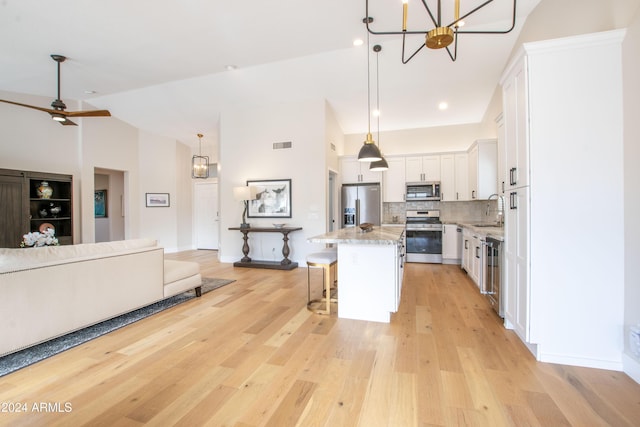 kitchen featuring a kitchen bar, appliances with stainless steel finishes, a kitchen island, decorative light fixtures, and white cabinetry