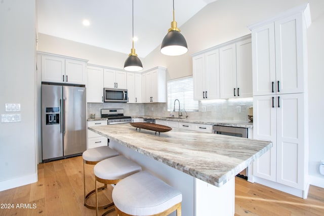 kitchen featuring white cabinetry, sink, decorative light fixtures, a kitchen island, and appliances with stainless steel finishes