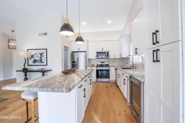 kitchen with appliances with stainless steel finishes, sink, white cabinets, a center island, and hanging light fixtures