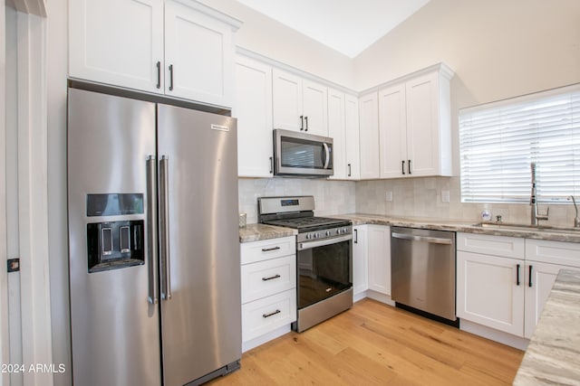 kitchen featuring appliances with stainless steel finishes, backsplash, light stone counters, sink, and white cabinets