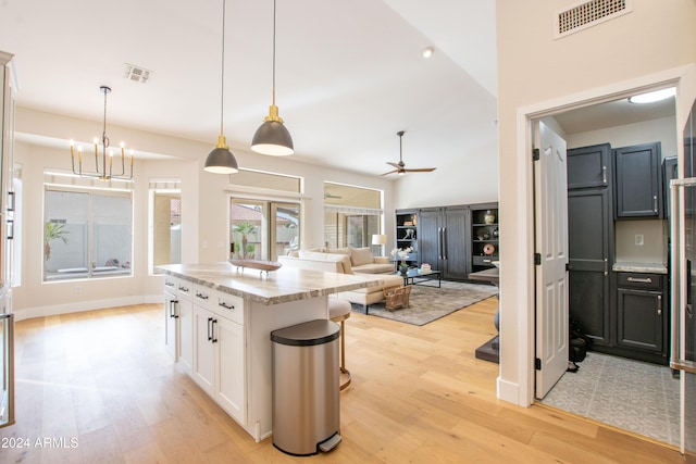 kitchen with white cabinets, decorative light fixtures, light stone counters, and ceiling fan with notable chandelier