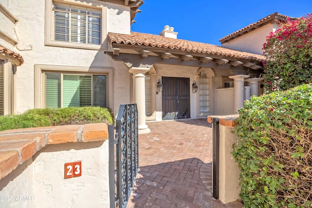 entrance to property with a chimney, a tile roof, a gate, and stucco siding