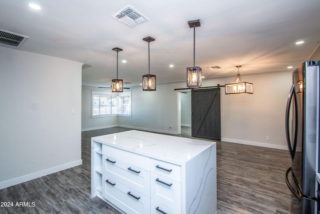 kitchen featuring light stone counters, pendant lighting, stainless steel fridge, white cabinetry, and a barn door