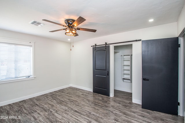 unfurnished bedroom with a closet, ceiling fan, dark wood-type flooring, and a barn door