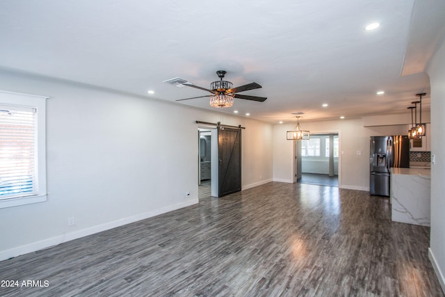 unfurnished living room with a barn door, a healthy amount of sunlight, dark hardwood / wood-style flooring, and ceiling fan