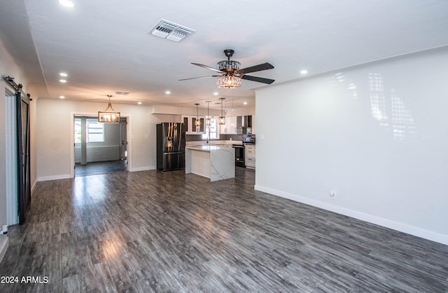 unfurnished living room with dark hardwood / wood-style flooring, ceiling fan, and a barn door