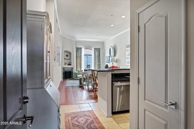 kitchen featuring dark countertops, ornamental molding, open floor plan, stainless steel dishwasher, and light tile patterned flooring