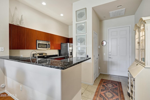 kitchen featuring visible vents, dark stone counters, appliances with stainless steel finishes, a peninsula, and light tile patterned flooring