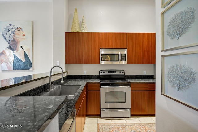 kitchen featuring stainless steel appliances, dark stone counters, brown cabinetry, and a sink