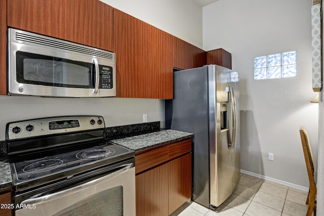 kitchen with stainless steel appliances, baseboards, dark stone countertops, and light tile patterned floors