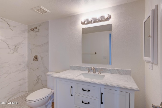 bathroom featuring a marble finish shower, visible vents, a textured wall, toilet, and vanity