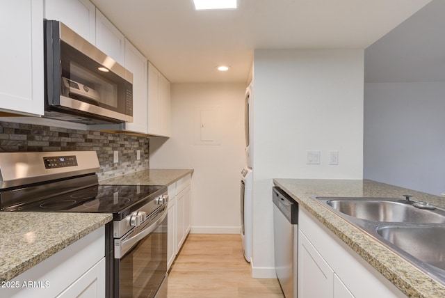 kitchen with stacked washer and dryer, a sink, white cabinetry, appliances with stainless steel finishes, and tasteful backsplash