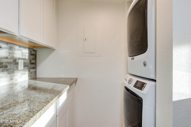 clothes washing area with electric panel, cabinet space, and stacked washer / drying machine