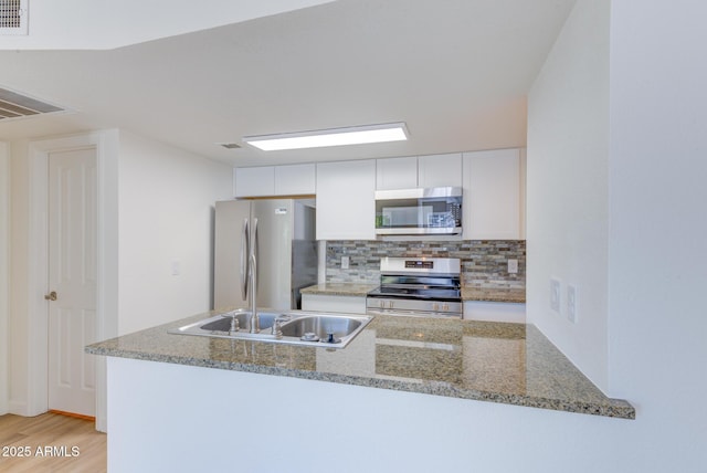 kitchen featuring tasteful backsplash, white cabinets, light stone counters, appliances with stainless steel finishes, and a sink