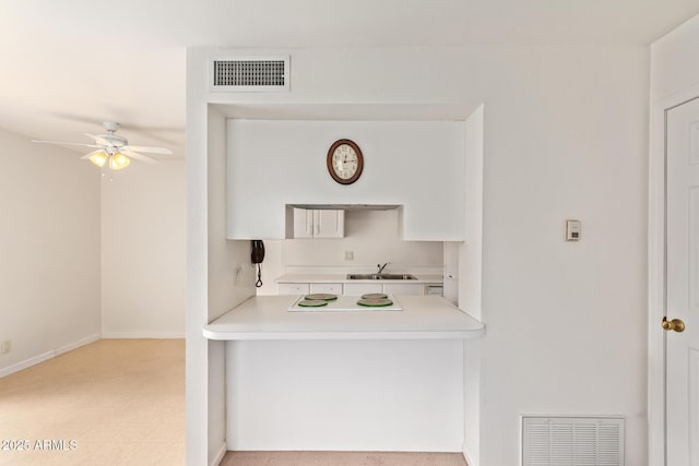 kitchen with a ceiling fan, a sink, light countertops, baseboards, and white cabinets