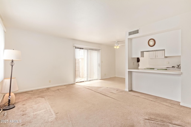 unfurnished living room with carpet flooring, a sink, a ceiling fan, and baseboards