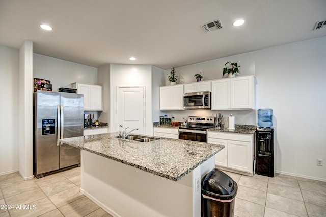 kitchen featuring stainless steel appliances, visible vents, white cabinetry, light stone countertops, and an island with sink