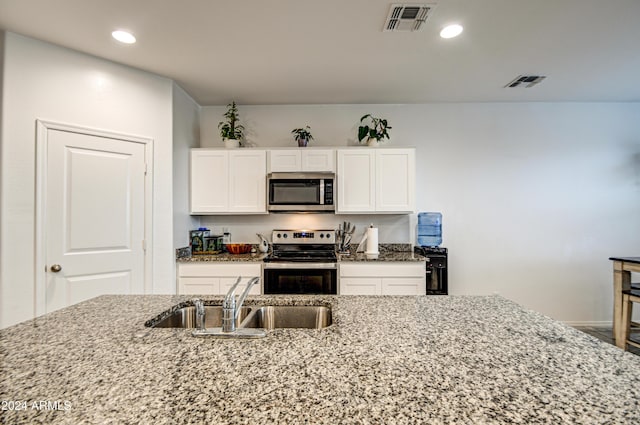 kitchen with light stone counters, stainless steel appliances, visible vents, white cabinets, and a sink