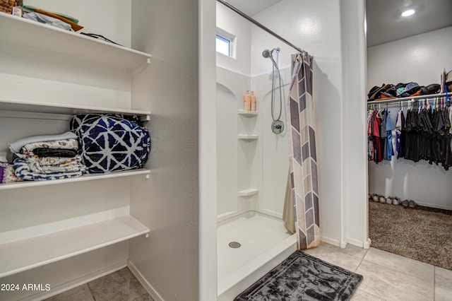 bathroom with baseboards, a spacious closet, a shower stall, and tile patterned floors