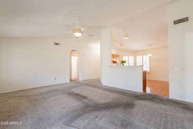 carpeted spare room featuring vaulted ceiling, arched walkways, a ceiling fan, and visible vents