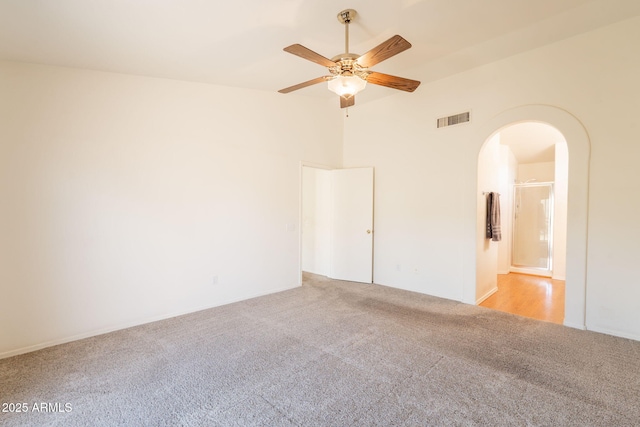 spare room with a ceiling fan, arched walkways, light colored carpet, and visible vents