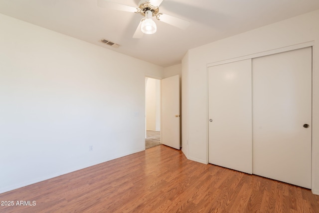 unfurnished bedroom with a ceiling fan, visible vents, wood finished floors, and a closet