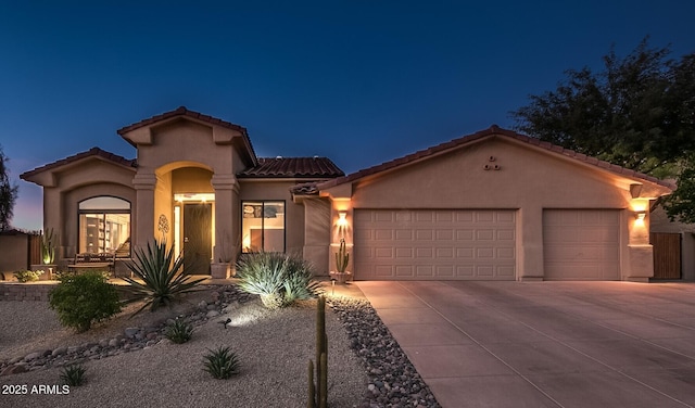 mediterranean / spanish-style home featuring driveway, an attached garage, a tiled roof, and stucco siding