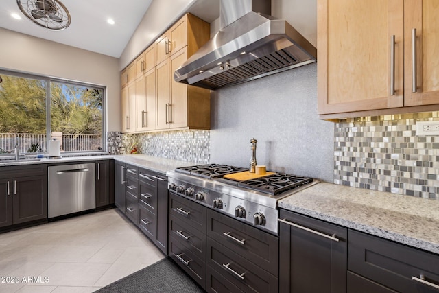 kitchen featuring light tile patterned floors, decorative backsplash, appliances with stainless steel finishes, light stone counters, and wall chimney range hood