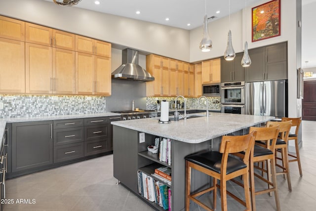 kitchen featuring tasteful backsplash, a towering ceiling, stainless steel appliances, wall chimney range hood, and a sink