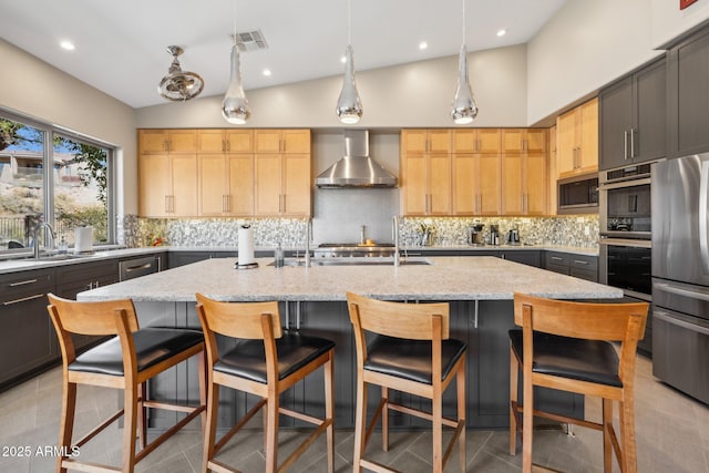 kitchen with stainless steel appliances, visible vents, backsplash, a sink, and wall chimney exhaust hood