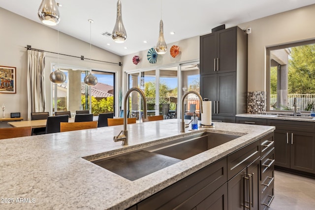 kitchen featuring light stone countertops, visible vents, pendant lighting, and a sink