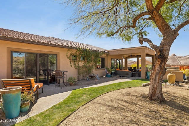 rear view of house with a patio area, a tile roof, and stucco siding