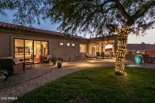 rear view of property with a patio, a tile roof, a yard, outdoor lounge area, and stucco siding