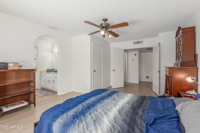 2031 W Gila Ln, Chandler, AZ 85224 - bedroom featuring light wood finished floors, arched walkways, a textured ceiling, connected bathroom, and a ceiling fan