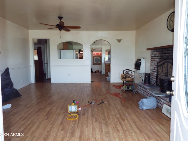 unfurnished living room with a brick fireplace, wood-type flooring, heating unit, and ceiling fan