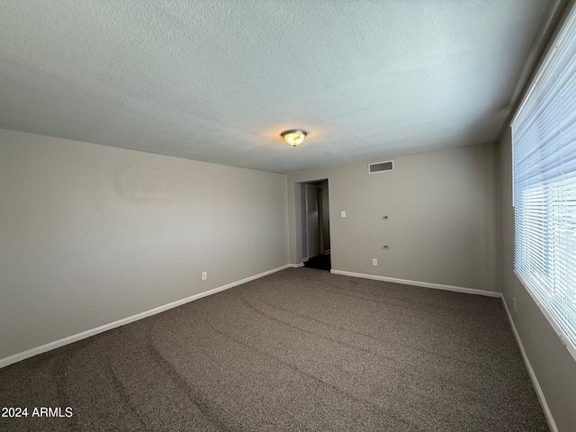 unfurnished room featuring a textured ceiling and dark carpet