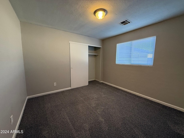 unfurnished bedroom featuring dark carpet, a textured ceiling, and a closet