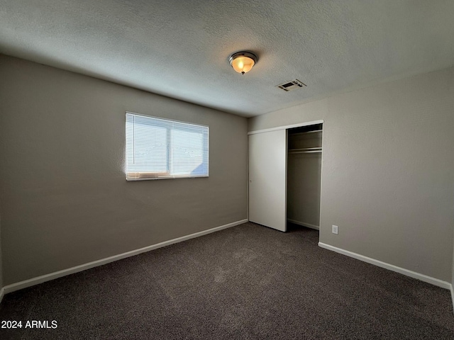 unfurnished bedroom featuring dark colored carpet, a textured ceiling, and a closet